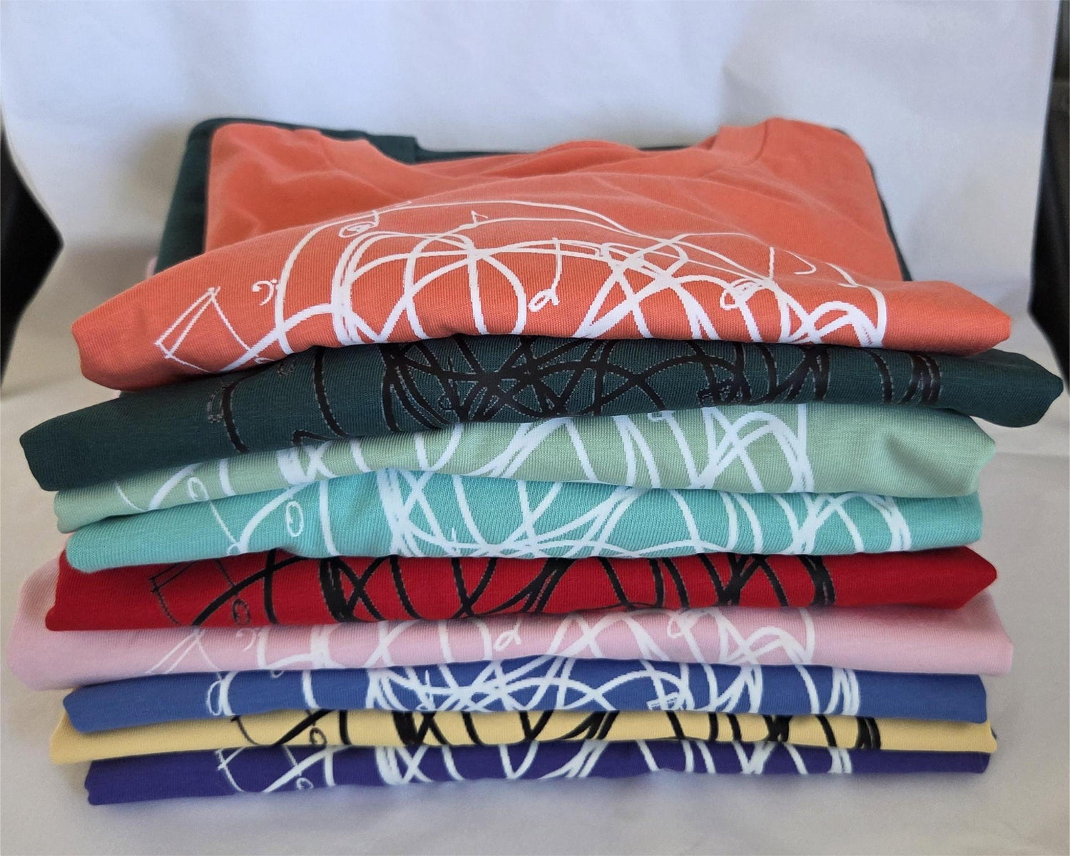 Stack of folded t-shirts with colorful abstract designs on a white background